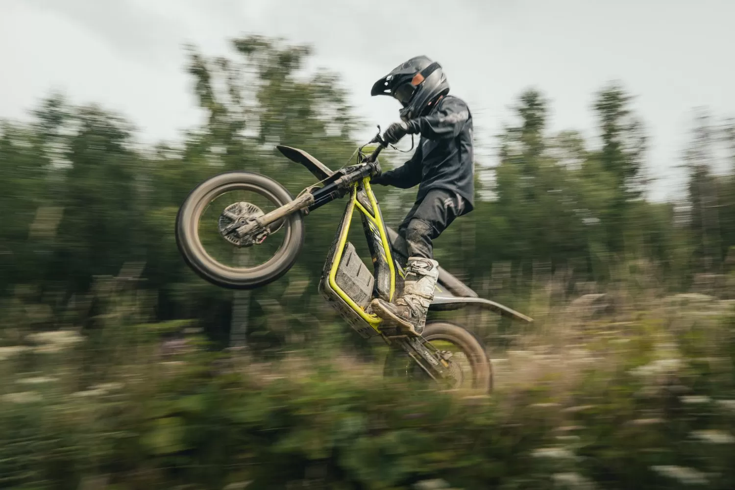 Triumph TXP-24 electric motorcycle riding near wooded trails
