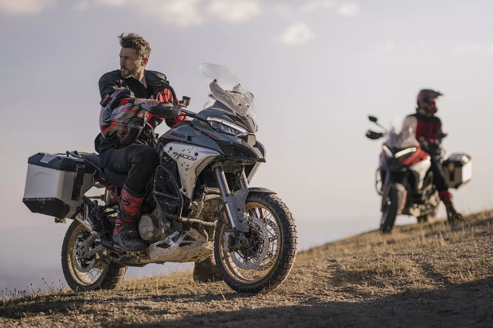 Rider standing beside the new Ducati Multistrada V4 Rally admiring a scenic view, with another Multistrada V4 in the background.