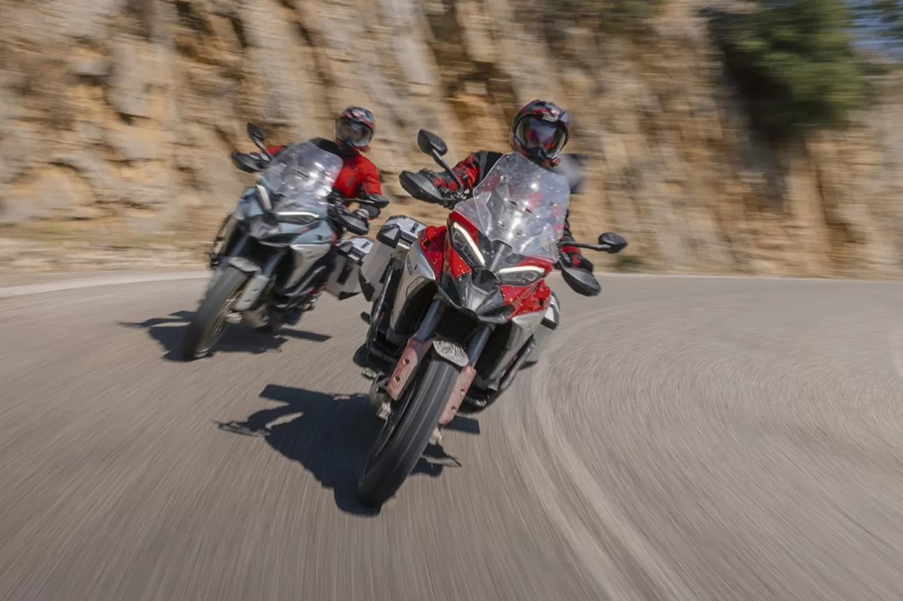 Two riders on Ducati Multistrada V4 Rally motorcycles navigating a twisting mountain road.