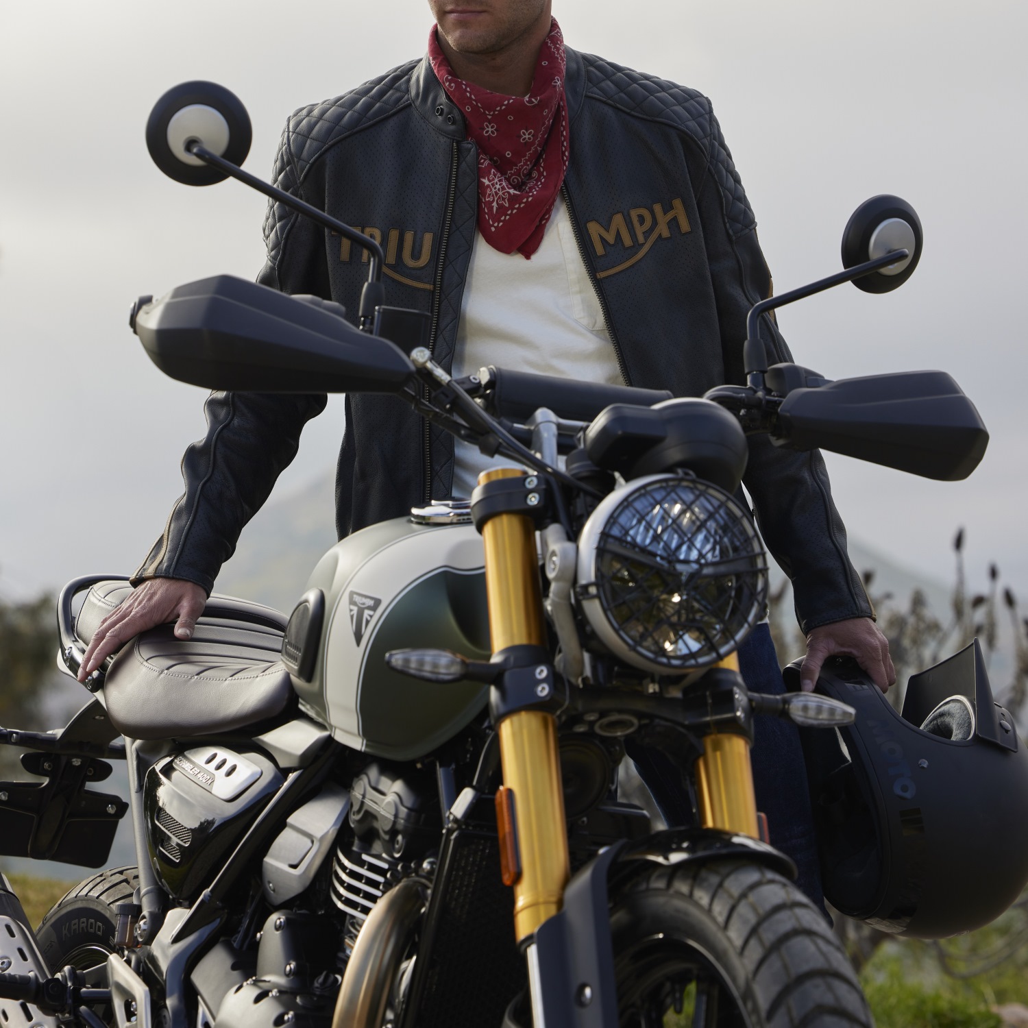 Man standing next to Triumph Scrambler 400 X holding a helmet